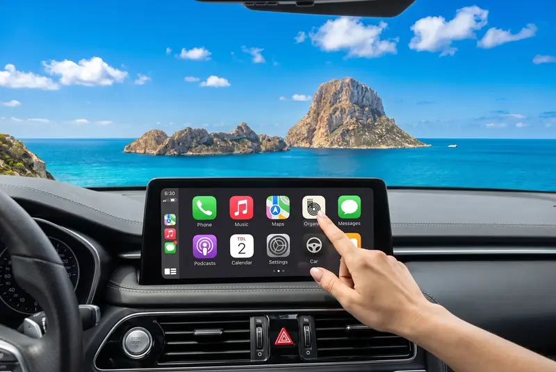 Autoscherm met Organica live in CarPlay, met uitzicht op Es Vedrà bij zonsondergang